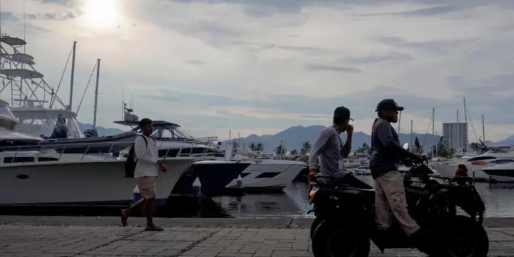 Personas caminan frente a embarcaciones en el muelle de la Marina ayer viernes, en Puerto Vallarta (México). EFE/Arturo Montero